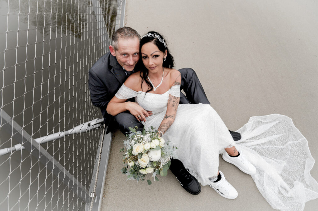 Brautpaar sitzt am Zaun – Hochzeitsfotografie by Jo