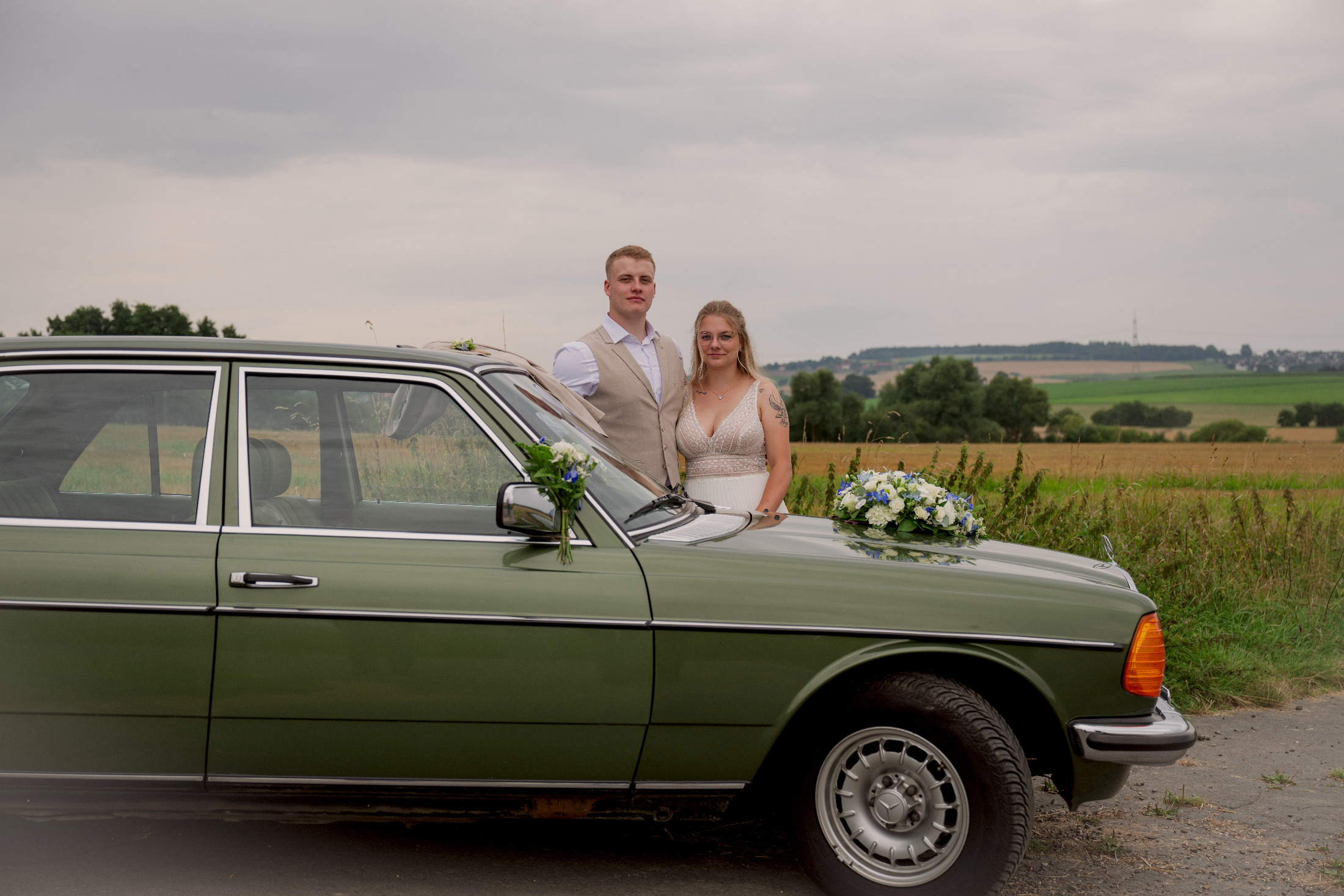 Brautpaar mit grünem Oldtimer im Feld – Hochzeitsfotografie by Jo